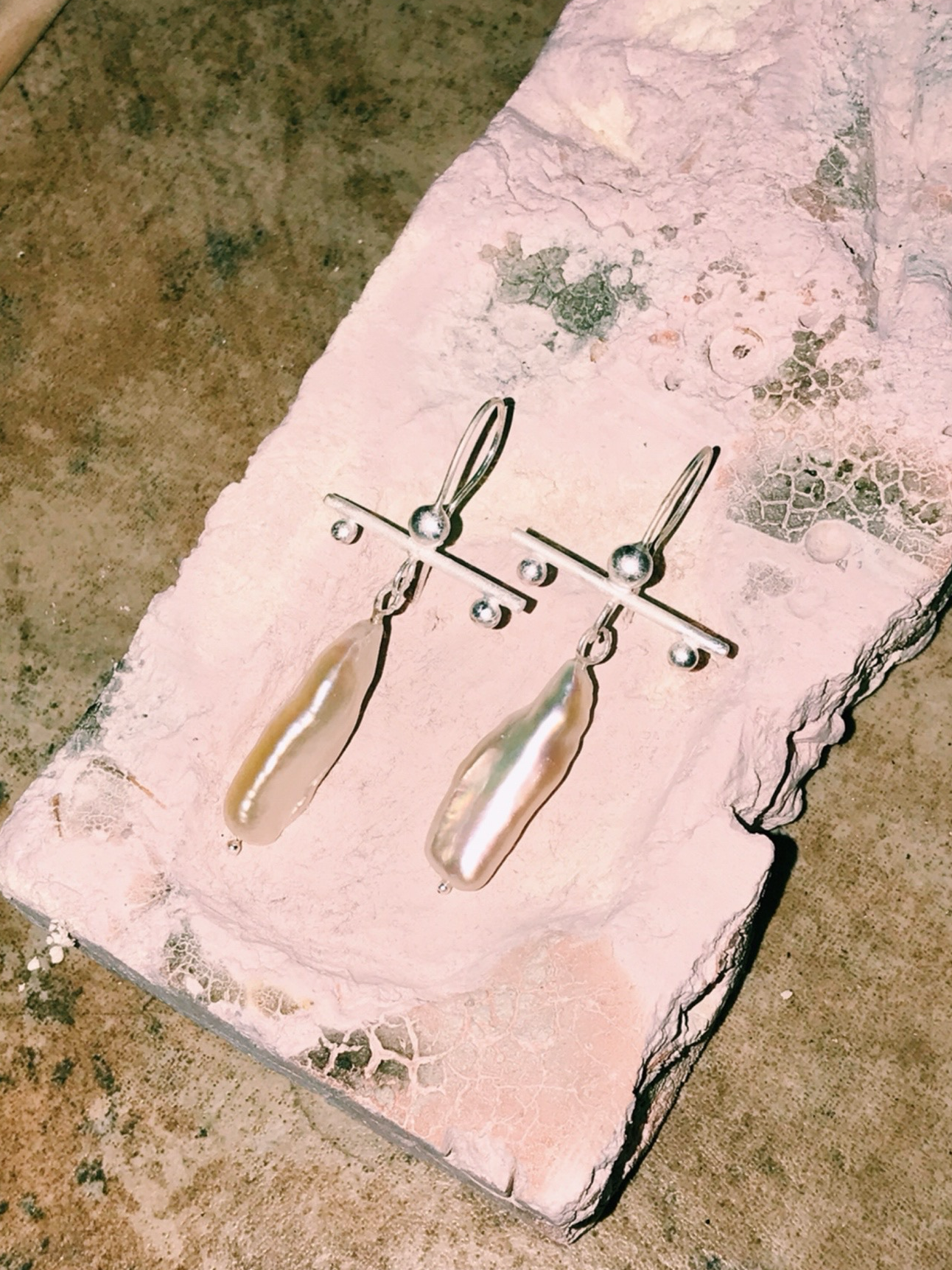 photograph of a pair of baroque pearl silver earrings designed and handmade by me. They have a T shaped where the horizontal part is made of silver wires with silver dots as adornment and the vertical part is a long baroque pearl.