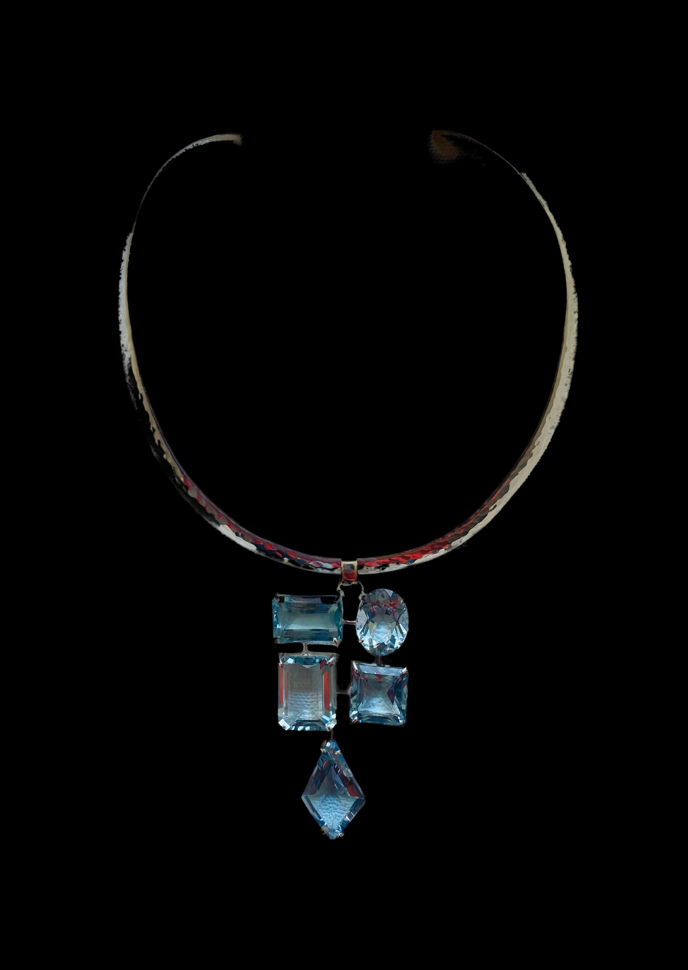 Photograph of a silver choker necklace, designed by me.The Pendant is a rhythmic mosaic of aquamarine stones faceted in various shapes on a black background.